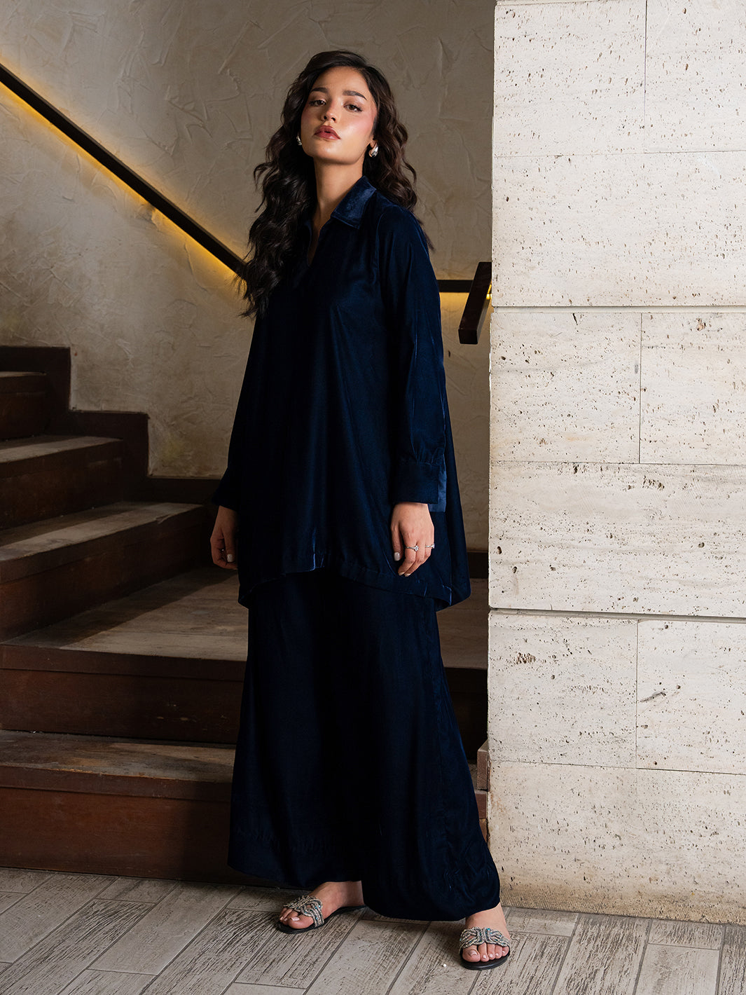 Woman in a navy blue outfit standing on a staircase with a neutral wall background